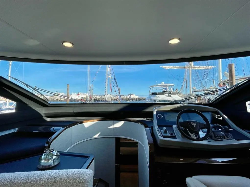 Interior view of a luxury yacht cockpit, overlooking the marina with boats and a clear blue sky visible through the glass.